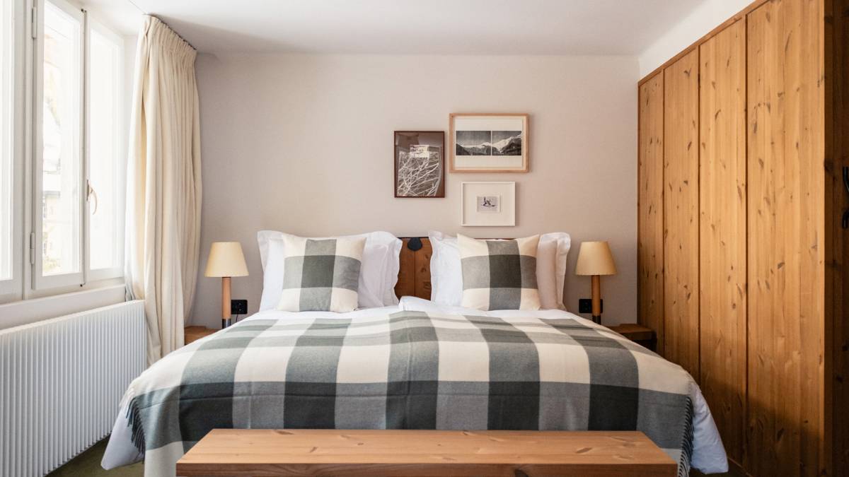 A well-organized bedroom features a cozy bed, two side tables with lamps, and mounted portraits.