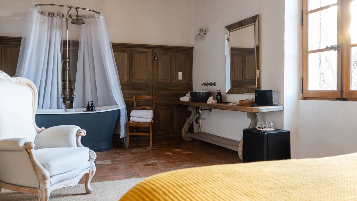 A properly arranged bedroom featuring a cozy bed, bathtub in left corner, and cozy chair.